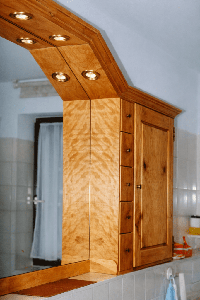Waschbeckenoberschrank aus massiver, geflammter Birke mit Hartöloberfläche, handgezinkte Schübe, gezapfte Rahmentüren mit glatten, innen abgeschrägten Füllungen, Messingscharniere, integrierter Spiegel mit fünf Einbauleuchten.